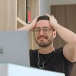 a man with glasses is looking at a laptop